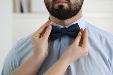 Woman adjusting bow tie to man indoors, closeup