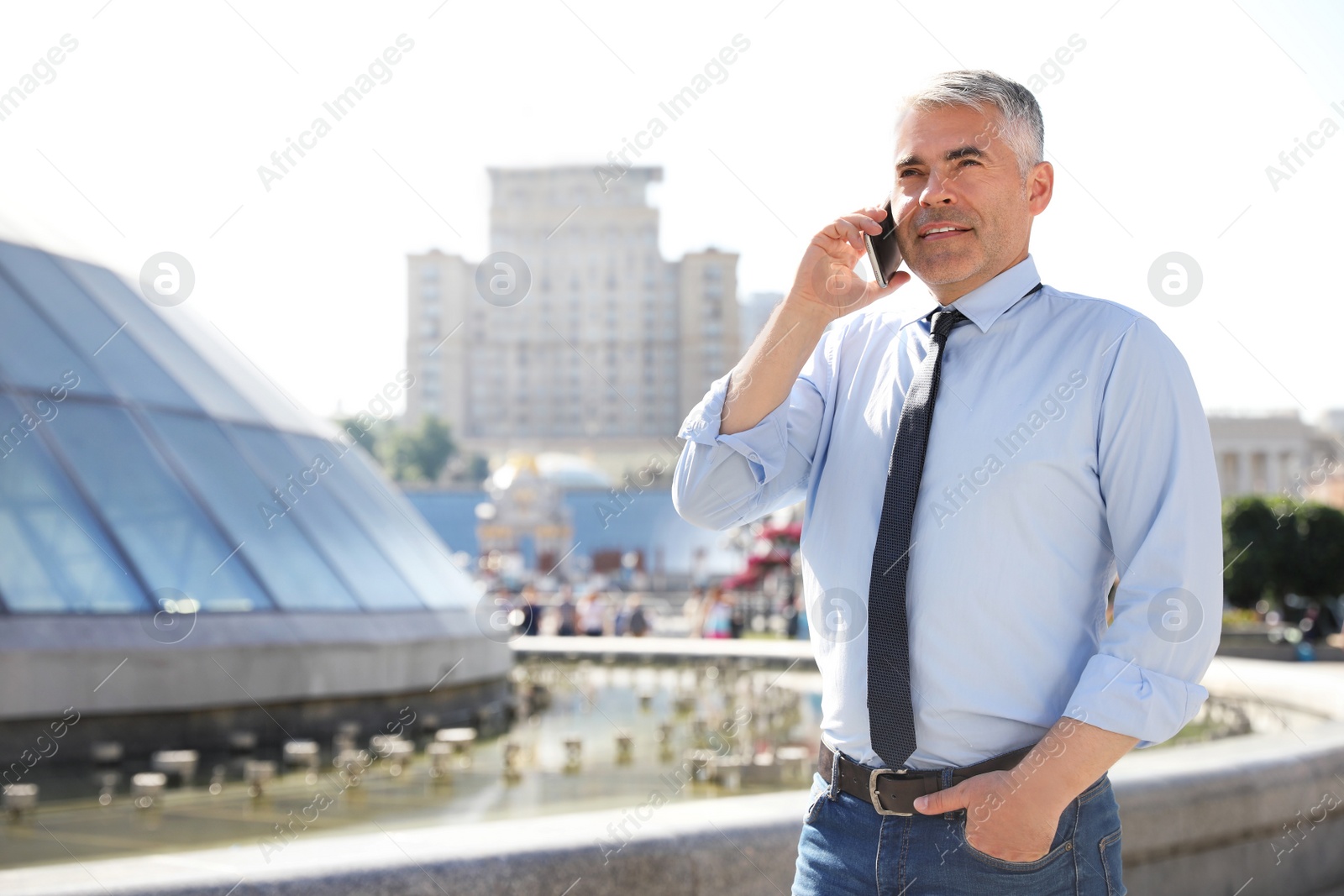 Photo of Handsome businessman talking by mobile phone in city, space for text