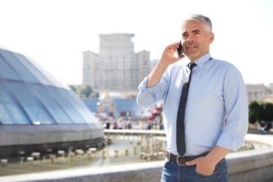 Photo of Handsome businessman talking by mobile phone in city, space for text