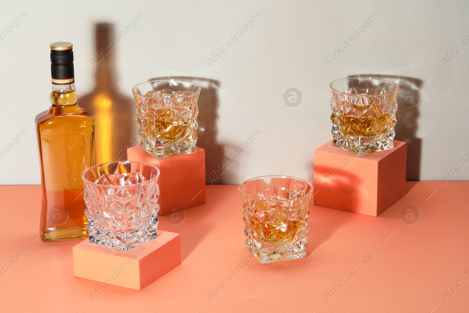 Photo of Stylish presentation of whiskey with ice cubes in glasses and bottle on color background