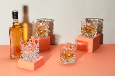 Stylish presentation of whiskey with ice cubes in glasses and bottle on color background