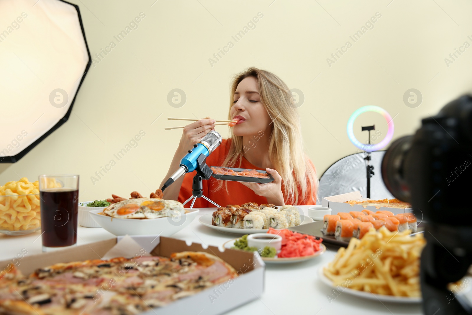 Photo of Food blogger recording eating show on camera against light background. Mukbang vlog