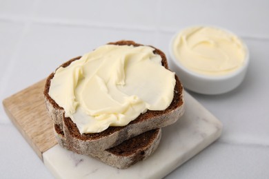 Photo of Slices of tasty bread with butter on white tiled table, closeup