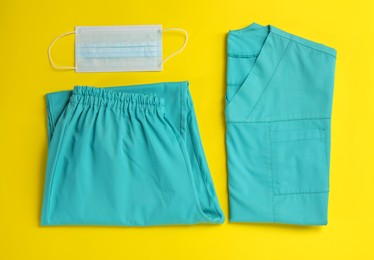 Photo of Medical uniform and face mask on yellow background, flat lay