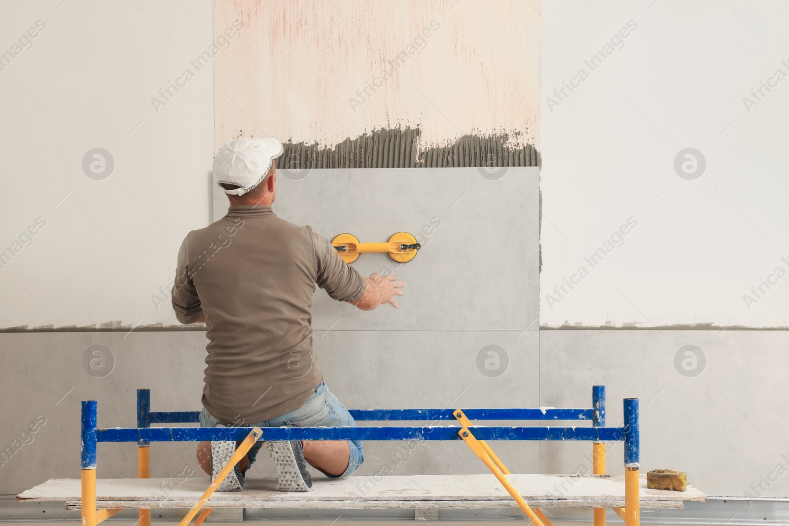 Photo of Worker installing tile on wall indoors, back view