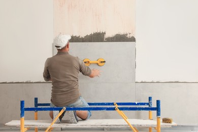 Worker installing tile on wall indoors, back view