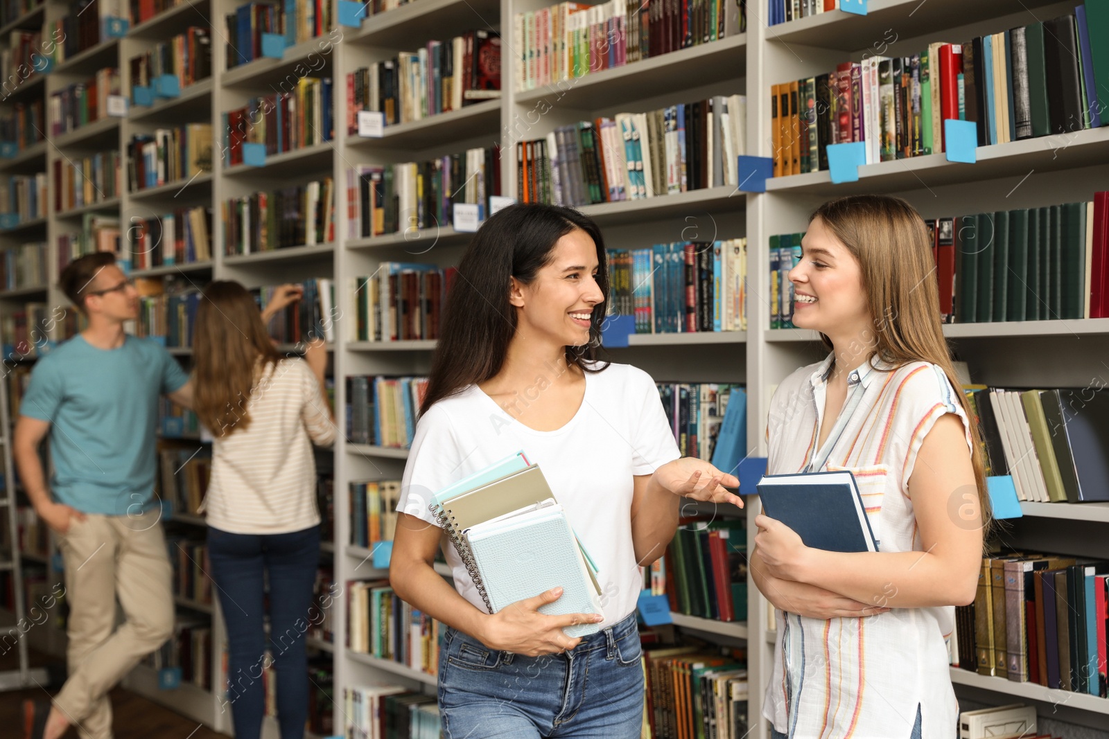 Photo of Young people standing near bookshelves in library