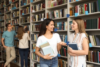 Young people standing near bookshelves in library