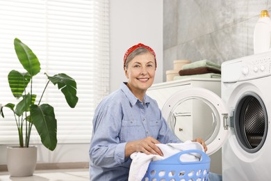 Happy housewife with laundry basket near washing machine at home