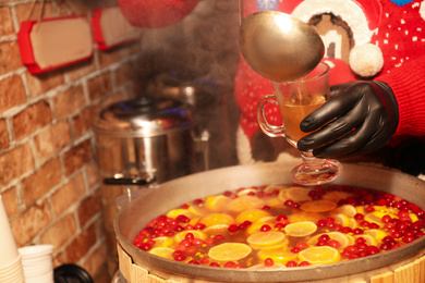 Seller pouring tasty mulled wine into cup at winter fair, closeup