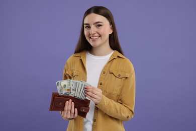 Photo of Happy woman holding wallet with dollar banknotes on purple background