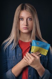 Photo of Sad woman holding Ukrainian flag on black background