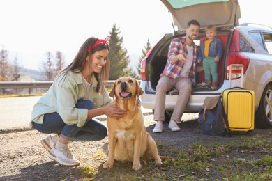 Photo of Happy woman petting dog, father and his daughter sitting in car trunk outdoors. Family traveling with pet