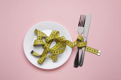 Photo of Measuring tape, fork and knife on pink background, flat lay. Weight loss concept