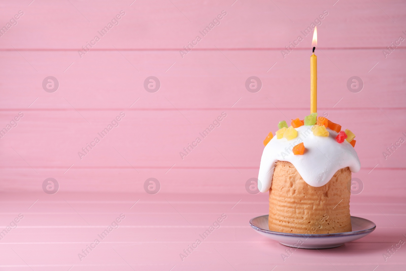 Photo of Easter cake with burning candle on pink wooden table, space for text