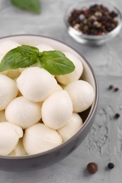 Photo of Tasty mozzarella balls and basil leaves in bowl on grey table, above view