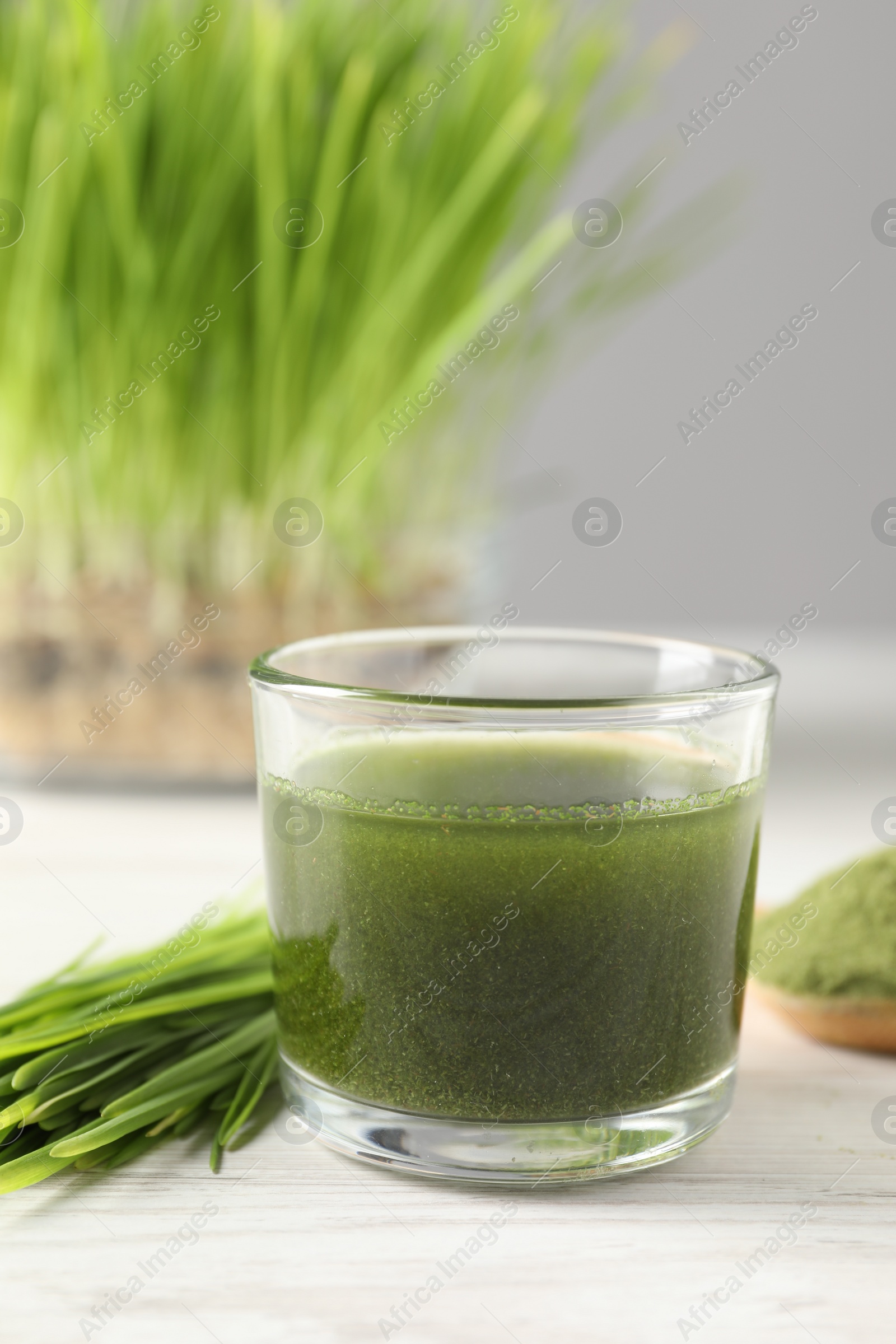 Photo of Wheat grass drink in glass and fresh sprouts on white wooden table, closeup