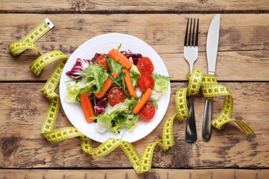 Photo of Plate with fresh vegetable salad and measuring tape on wooden table, flat lay. Healthy diet concept