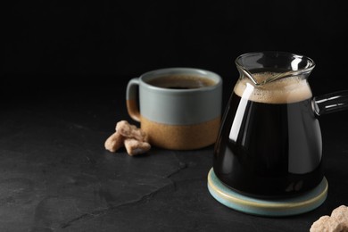 Photo of Turkish coffee in glass cezve and cup on dark grey table. Space for text