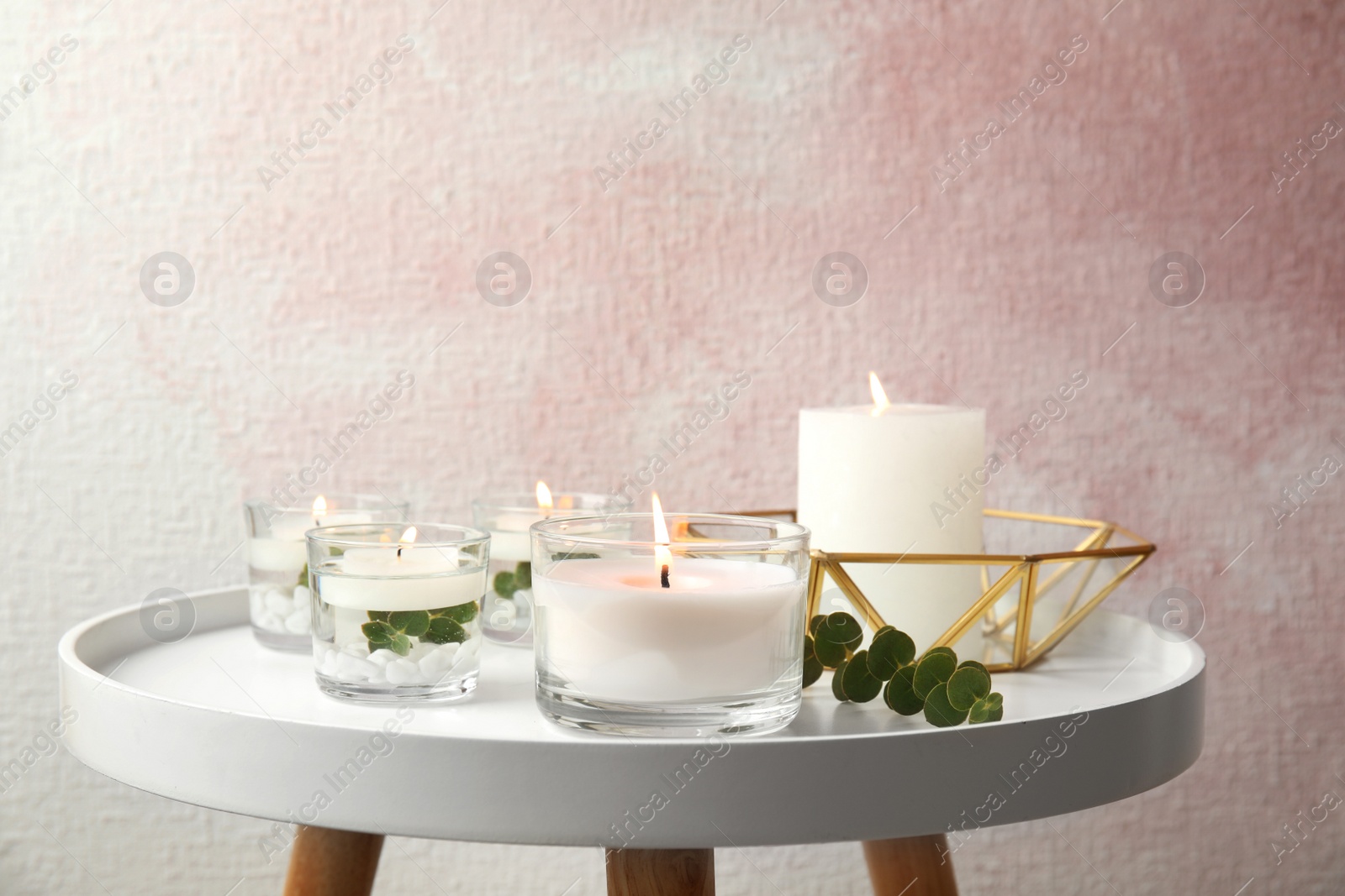 Photo of Composition with burning aromatic candles and eucalyptus on table near color wall. Space for text