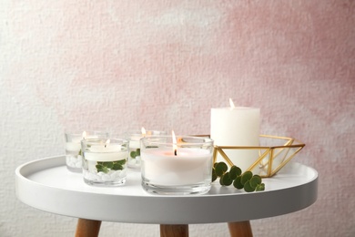 Composition with burning aromatic candles and eucalyptus on table near color wall. Space for text