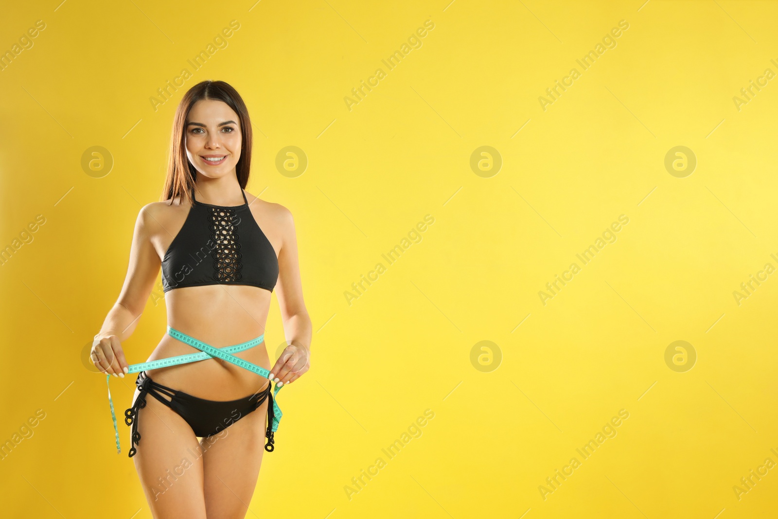 Photo of Attractive young woman with slim body measuring her waist on color background. Space for text