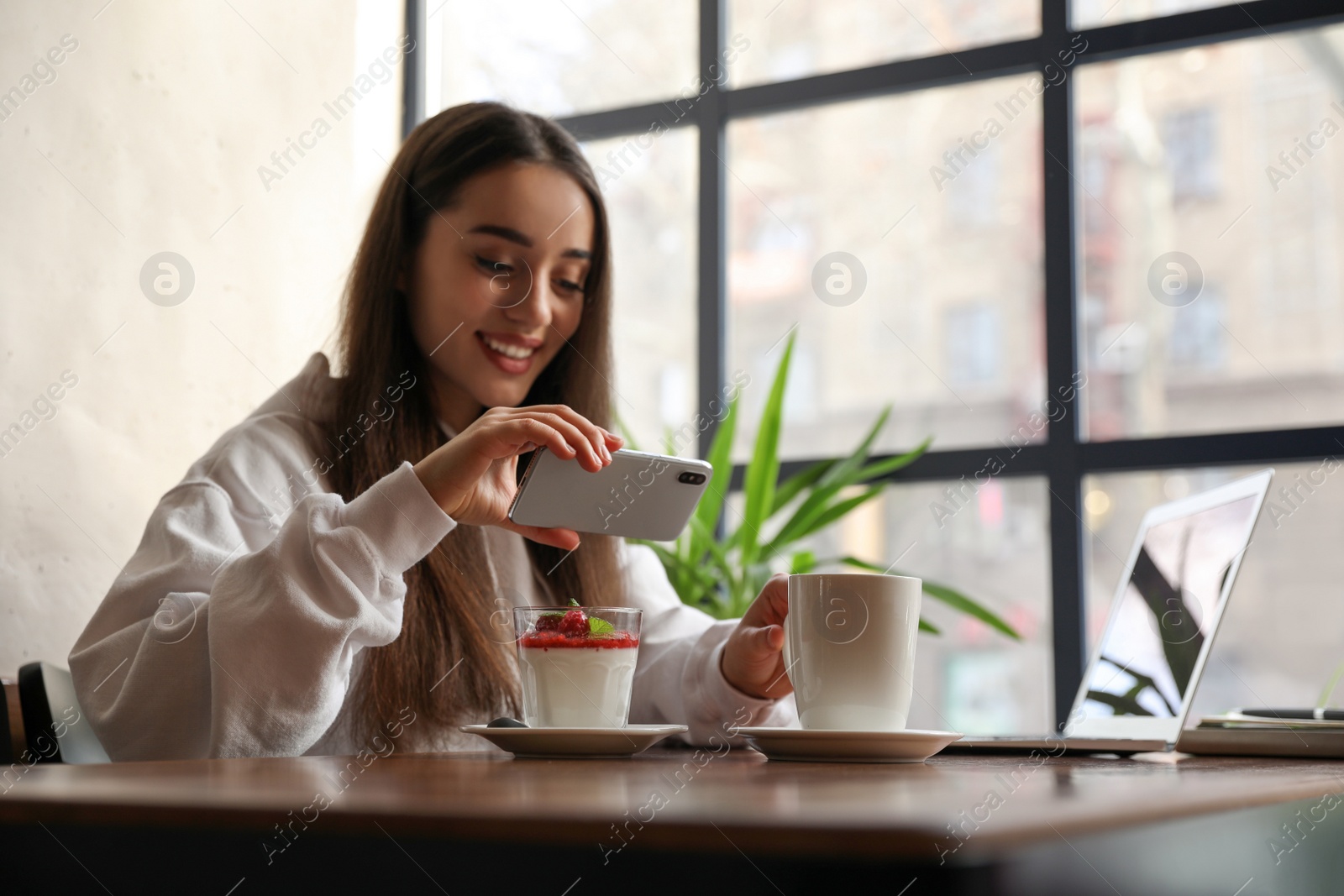 Photo of Young blogger taking picture of dessert at table in cafe