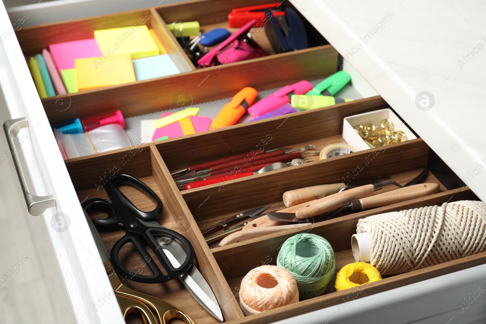 Photo of Sewing accessories and stationery in open desk drawer indoors, closeup