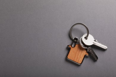 Photo of Keys with trinket in shape of house on grey background, top view and space for text. Real estate agent services