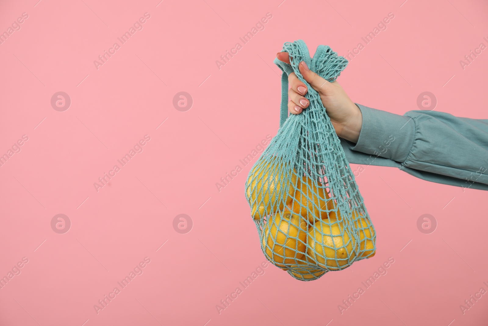 Photo of Woman with string bag of fresh lemons on pink background, closeup. Space for text