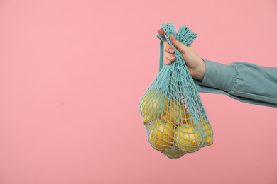 Photo of Woman with string bag of fresh lemons on pink background, closeup. Space for text