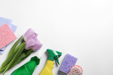 Photo of Spring cleaning. Detergents, flowers, sponge, brush and rag on white background, flat lay. Space for text