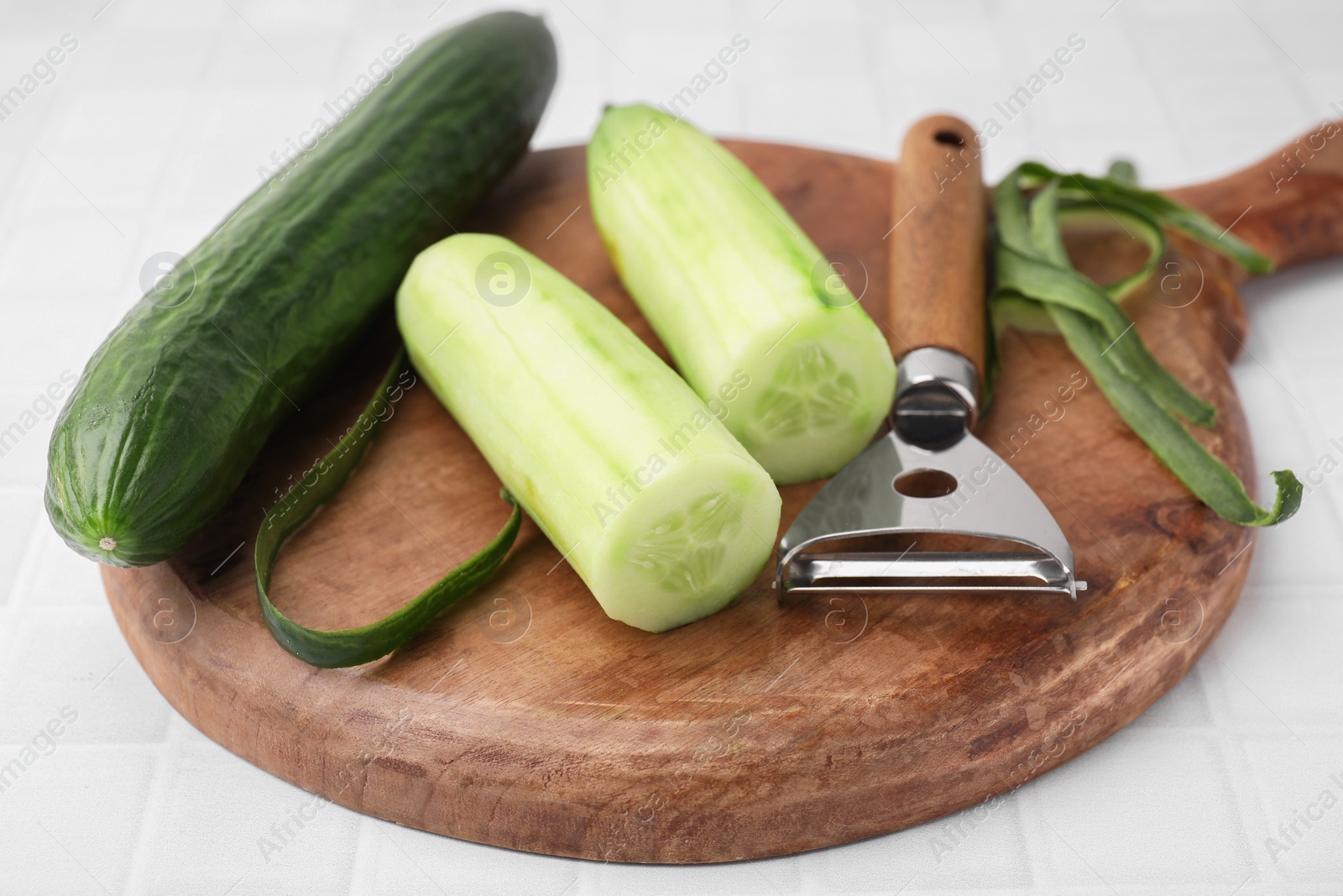 Photo of Fresh cucumbers and peeler on white tiled table, closeup