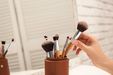 Photo of Professional makeup artist taking brush on dressing table, closeup