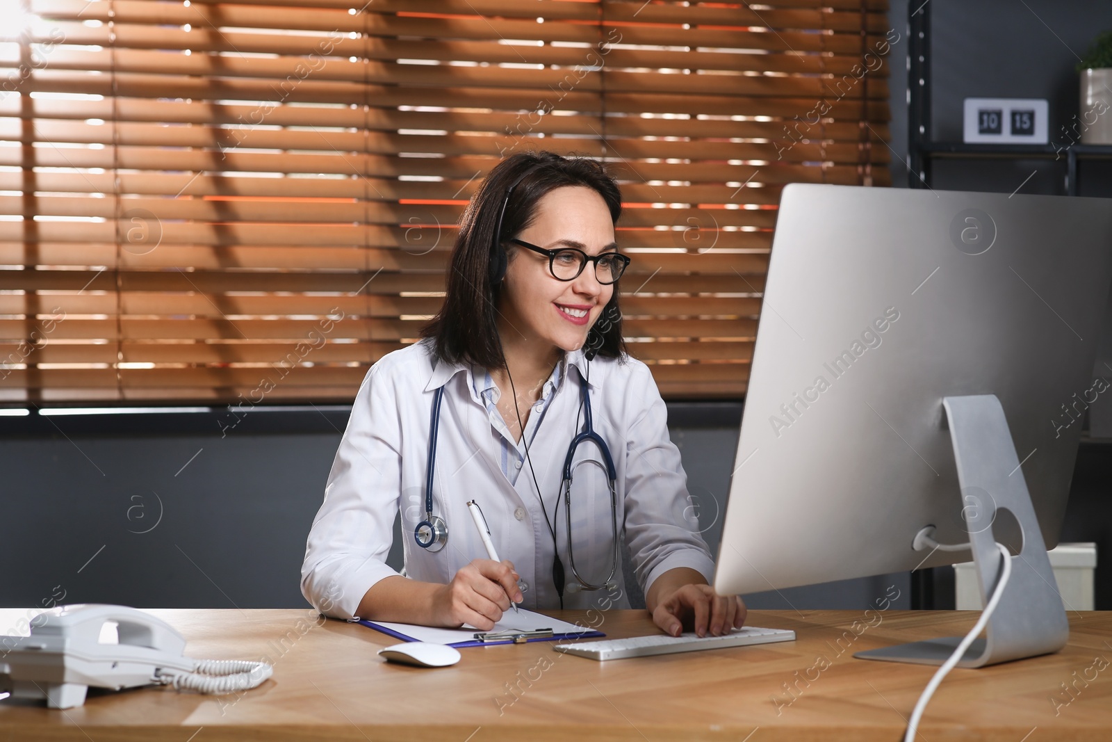 Photo of Doctor with headset and computer consulting patient online in office. Hotline service