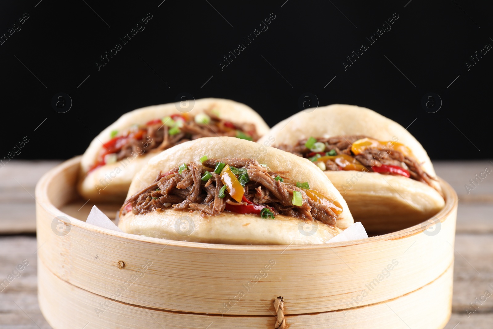 Photo of Delicious gua bao in bamboo steamer on wooden table, closeup