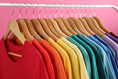 Photo of Rack with bright clothes on pink background. Rainbow colors