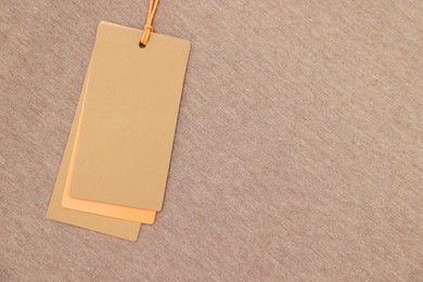 Cardboard tags on brown garment, top view. Space for text