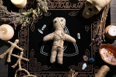 Photo of Voodoo doll pierced with pins surrounded by ceremonial items on table, flat lay. Curse ceremony
