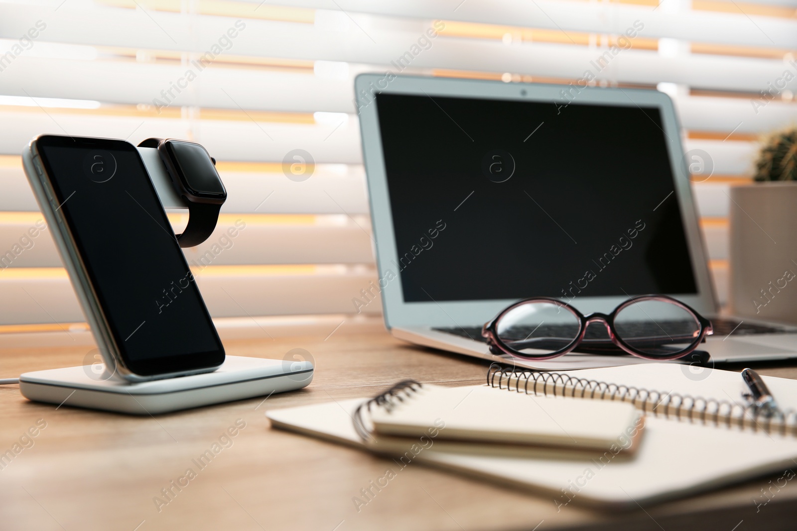 Photo of Mobile phone and smartwatch with wireless charger on wooden table. Modern workplace accessory