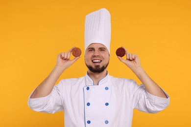 Photo of Happy professional confectioner in uniform holding delicious macarons on yellow background