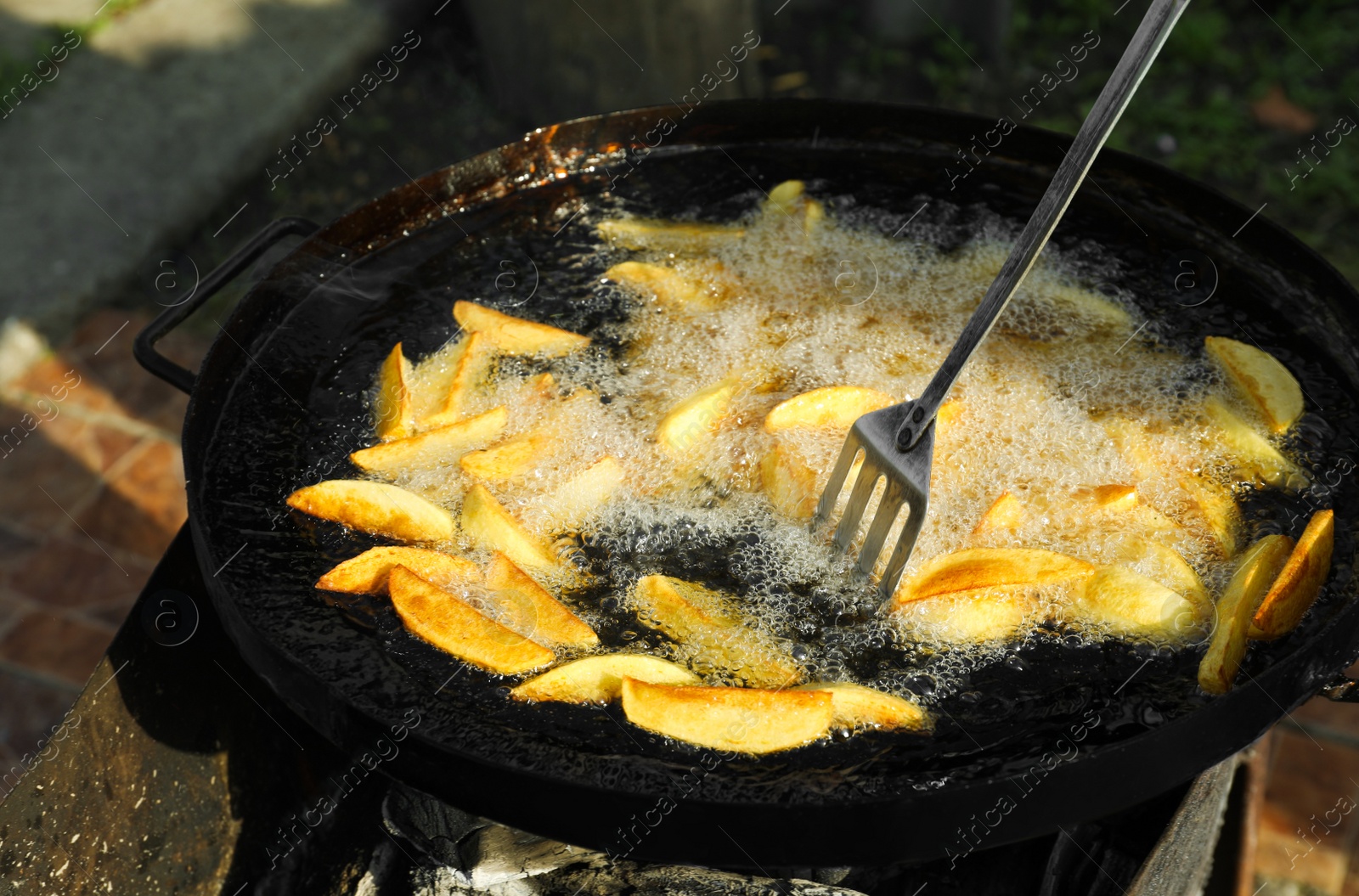 Photo of Cooking delicious potato wedges on frying pan outdoors