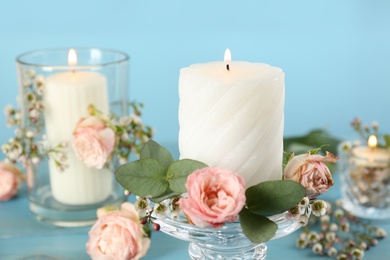 Photo of Glass candlestick with burning candles and floral decor on light blue table, closeup