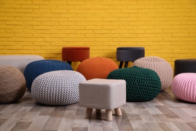 Many different stylish poufs on floor near yellow brick wall in room