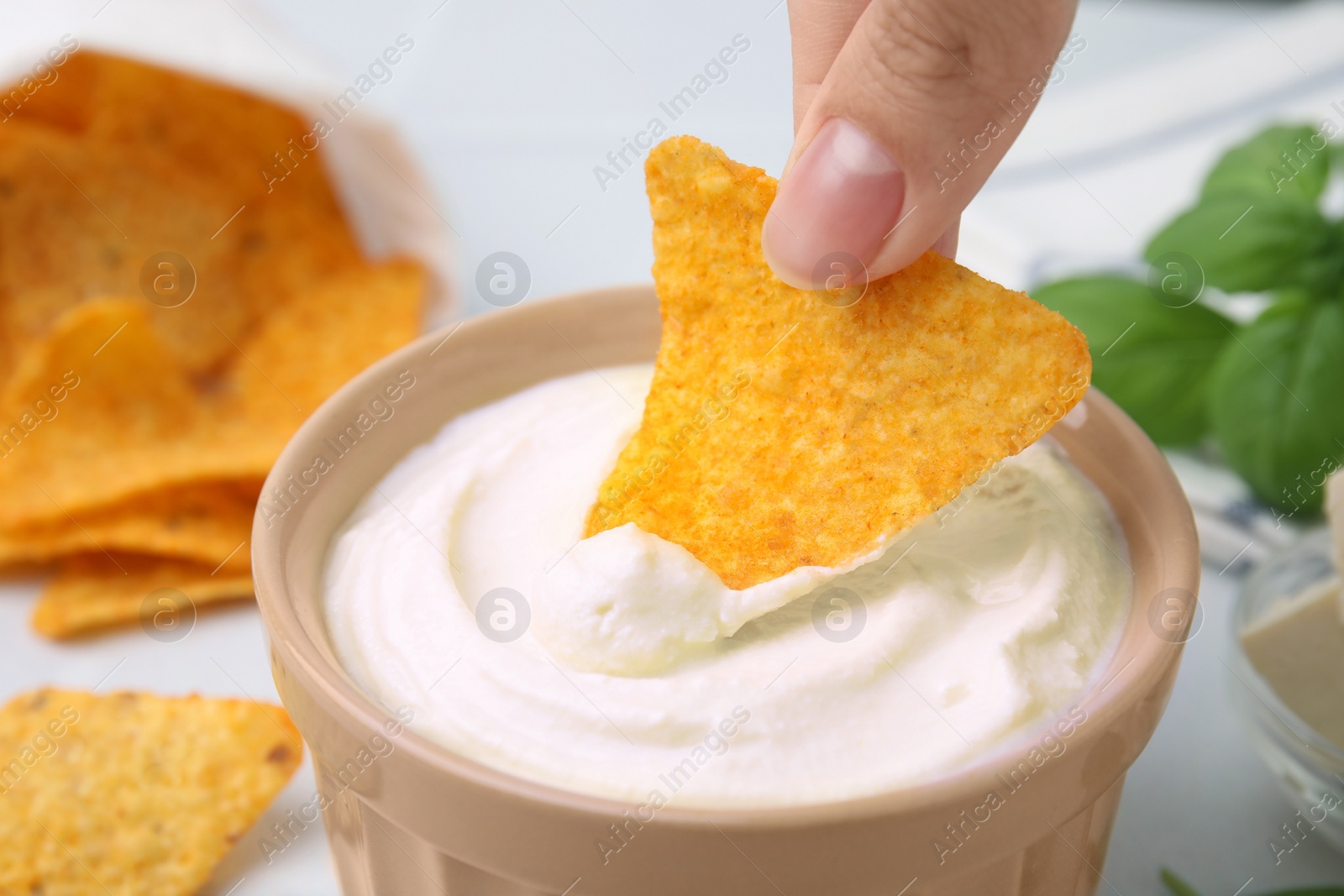 Photo of Woman dipping nachos chips into delicious tofu sauce at table, closeup
