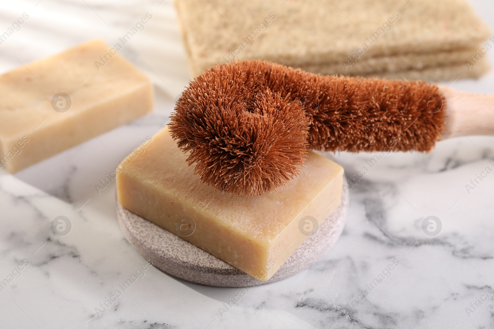 Photo of One cleaning brush and bar of soap on white marble table, closeup