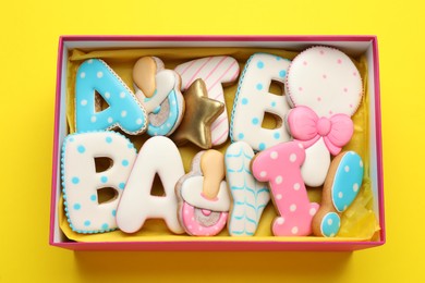Photo of Set of baby shower cookies in gift box on yellow background, top view