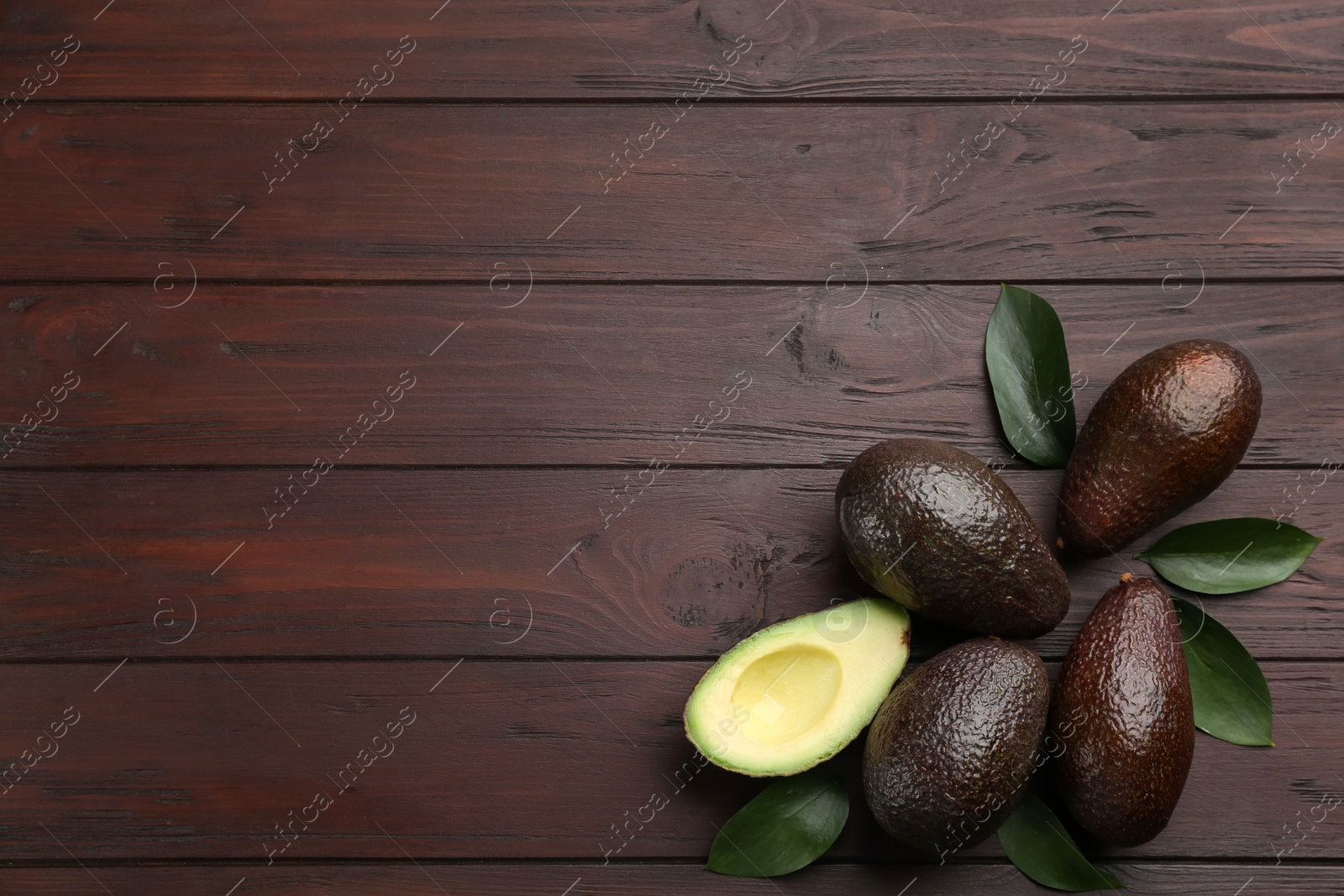 Photo of Whole and cut avocados with green leaves on wooden table, flat lay. Space for text