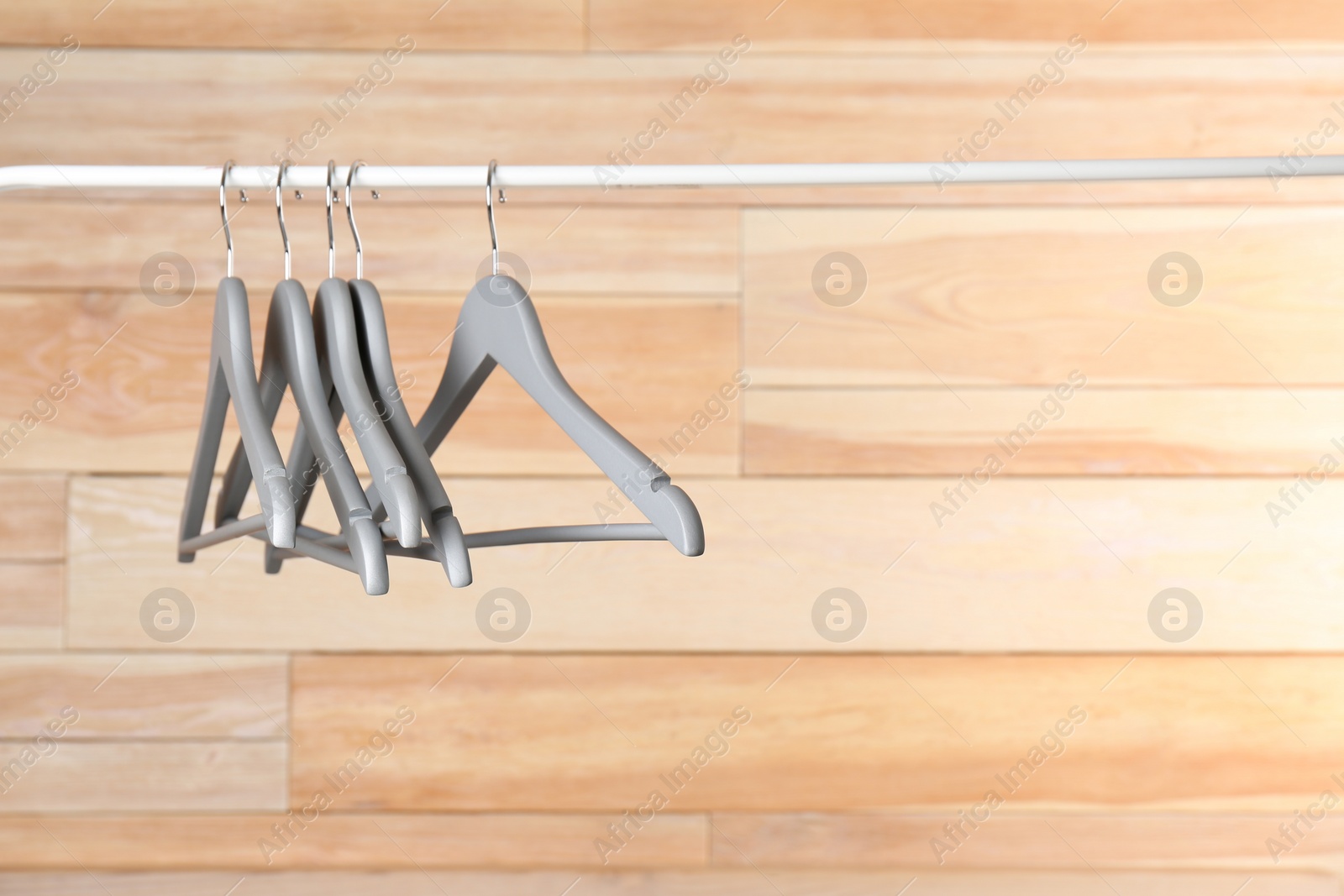 Photo of Metal rack with clothes hangers on wooden background, space for text