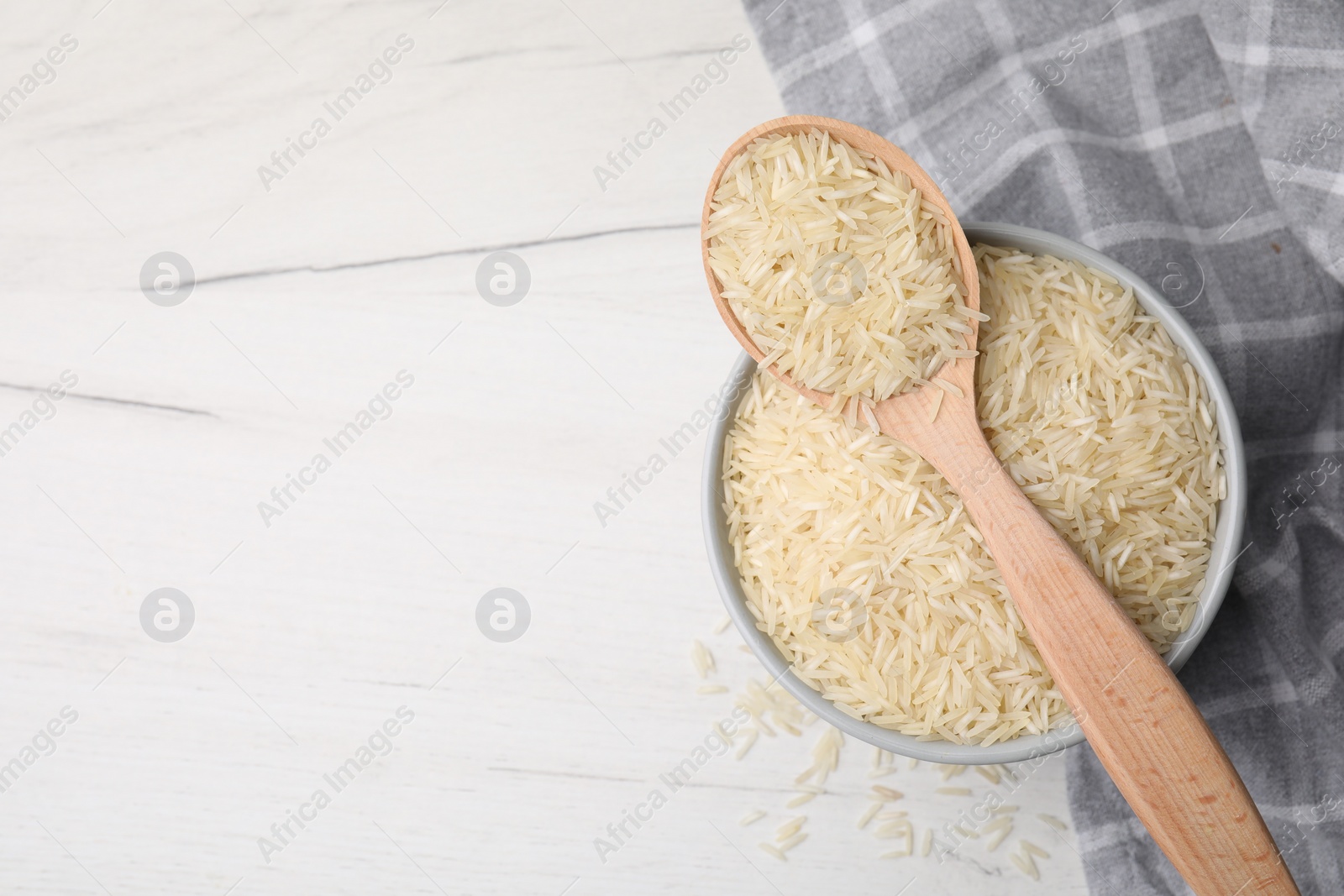 Photo of Bowl and spoon with raw rice on white wooden table, top view. Space for text